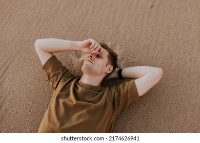 Young Man Laying In Beach Sand. People Fatigue From Sunburn And Work. Summer Sleeping And Relaxation Techniques. Vitamin D Sunbathing. Man Power Nap With Eye Closed. Rest After Work From Home