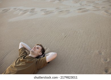 Young Man Laying In Beach Sand. People Fatigue From Sunburn And Work. Summer Sleeping And Relaxation Techniques. Vitamin D Sunbathing. Man Power Nap With Eye Closed. Rest In Heat Wave