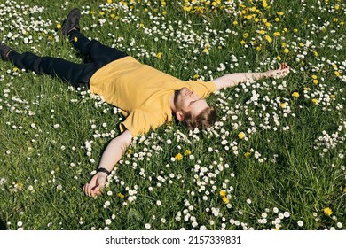 Young Man Laying In Green Grass With Flowers. People Fatigue From Work. Summer Sleeping And Relaxation Techniques. Vitamin D Sunbathing. Man Power Nap With Eye Closed. Rest After Work From Home