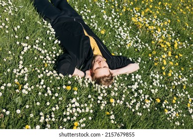 Young Man Laying In Green Grass With Flowers. People Fatigue From Work. Summer Sleeping And Relaxation Techniques. Vitamin D Sunbathing. Man Power Nap With Eye Closed. Rest After Work From Home