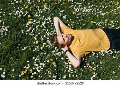 Young Man Laying In Green Grass With Flowers. People Fatigue From Work. Summer Sleeping And Relaxation Techniques. Vitamin D Sunbathing. Man Power Nap With Eye Closed. Rest After Work From Home