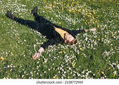 Young Man Laying In Green Grass With Flowers. People Fatigue From Work. Summer Sleeping And Relaxation Techniques. Vitamin D Sunbathing. Man Power Nap With Eye Closed. Rest After Work From Home