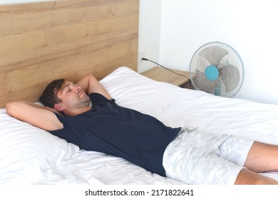 Young Man Laying And Sleeping Against Fan On A Hot Summer Day