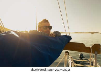 A young man leaning on the boom of a traditional gaff rig sailing boat at sunrise in Falmouth Harbour