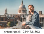 Young man leaning on railing of Millennium bridge. Male tourist looking away during vacation. Cathedral of St. Paul Church with clear blue sky in background on sunny day.