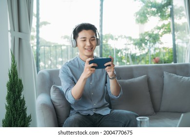 Young man leaning on sofa and playing games on phone at home