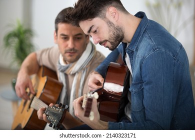 young man learning to play guitar with older male teacher