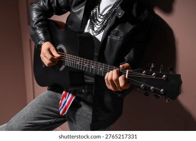 Young man in leather jacket playing guitar on brown background