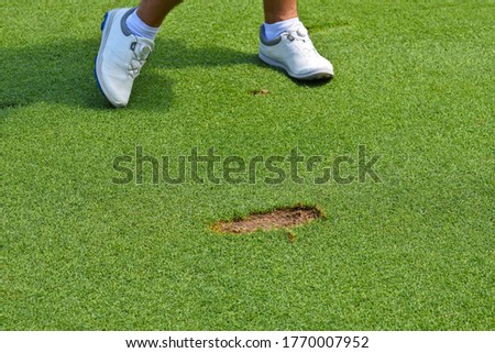 Young Man leaving a Divot cut out of the ground in the course of playing a stroke. 

 