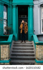 Young Man Leaving His House And Using His Smart Mobile With Colorful Houses On Portobello Street In The Notting Hill Neighborhood