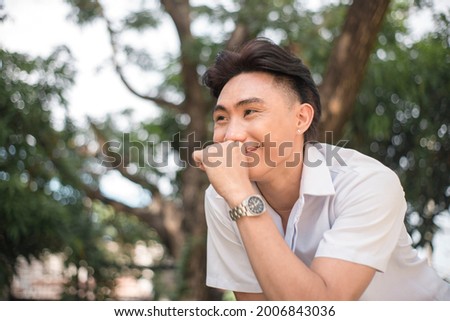 A young man lets out a subdued snicker while seeing someone or something funny for him. Outdoor scene.