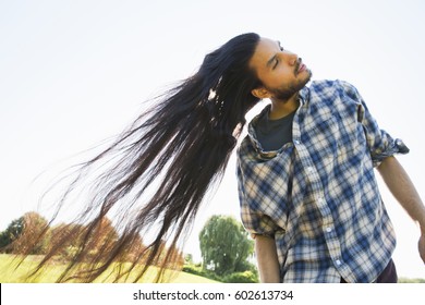 A young man letting down his very long dark hair and shaking his head to fan it out in the fresh air