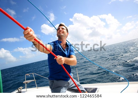 Young man lifting the sail of catamaran during cruising