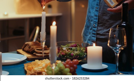Young man lighting the candle waiting her wife for a romantic dinner. Husband preparing festive meal with healty food for anniversary celebration, romantic date, sitting near the table in kitchen.