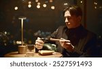 Young man lights cigar in restaurant. Media. Young man lights cigar with lighter in institution. Elegant man lights Cuban cigar in restaurant