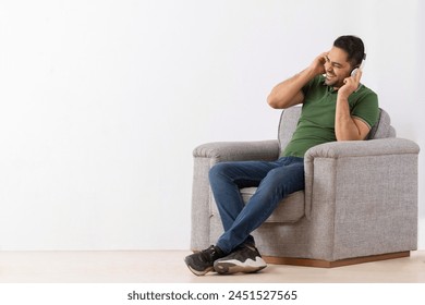 Young man listening music on headphones and having fun while sitting on sofa - Powered by Shutterstock