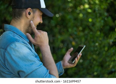 Young man listening to music with wireless earbuds and his smartphone. Technological concept