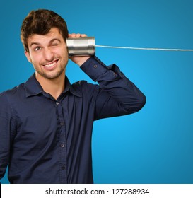 Young Man Listening From Tin Can Phone On Blue Background