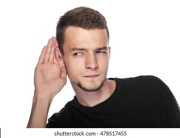 Young man listens putting hand to his ear. On white.