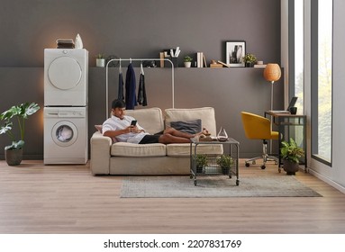 Young man is living at minimalist home style, working laptop, laundry, washing machine, looking phone at the room, grey wall background and decorative interior. - Powered by Shutterstock