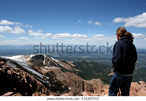 Young man with long hair looking out from on\
top of a mountain at a scenic view with the Continental Divide in\
background