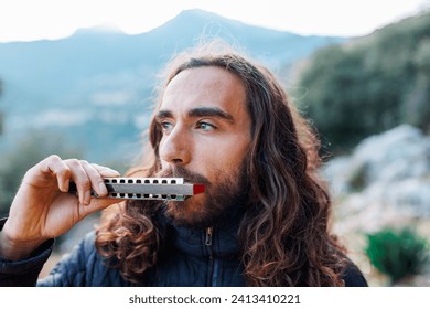 a young man with long hair plays the harmonica. a man enjoys playing the harmonica while standing on the street.