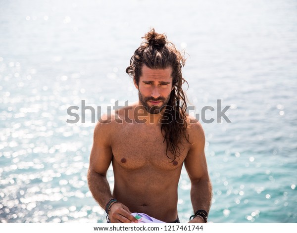 young man with long hair posing next to the coast\
showing his body