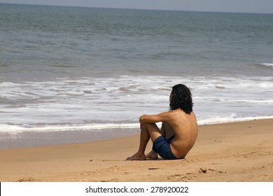 The young man with long hair sits on the coast and looks at the sea. India Goa. - Powered by Shutterstock