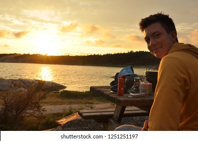 young man looking back at camera at seaside golden sunset with camping cooking gear on the table