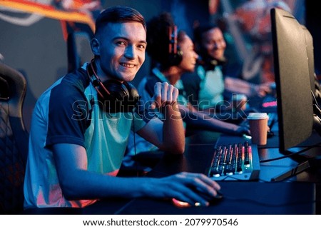 Young man looking at camera and smiling while sitting in gaming chair in interior of dark cyber sports club