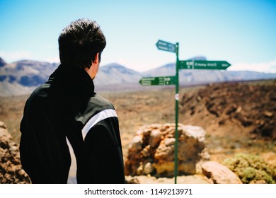 Young Man Looking In The Crossroad Sign On The Hiking Path