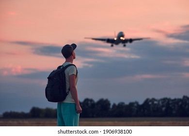 Young Man Looking Up At Flying Airplane Against Moody Sky During Dusk. Themes Nostalgia For Travel And Aviation.