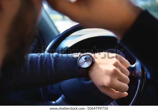 Young man looking at his watch in car during\
traffic jam, closeup