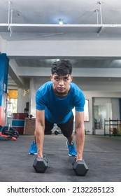 A young man looking intensely at the camera while training at the gym. Preparing to do Renegade rows or pushup variation with hex dumbbells.