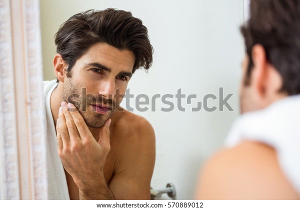 Young man looking in mirror and checking his\
stubble in bathroom