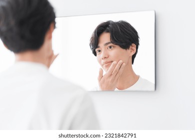 A young man is looking in the mirror and touching his face. - Powered by Shutterstock