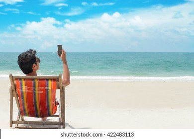 Young Man Looking At News And Messaging On His Smart Phone At Beach