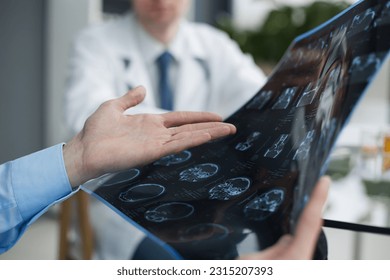 Young man looking at one of x-ray results being shown by his doctor - Shutterstock ID 2315207393