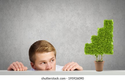 Young Man Looking Out On Tree In Pot From Under The Table