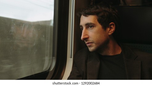 Young Man Looking Out Window While Riding And Commuting By Train