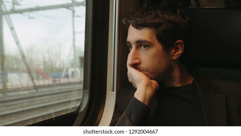 Young Man Looking Out Window While Riding And Commuting By Train