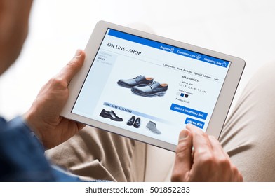 Young man looking at shoes online. Man looking at various shoes options over internet through digital tablet. Casual man makes online shopping at home with digital tablet.