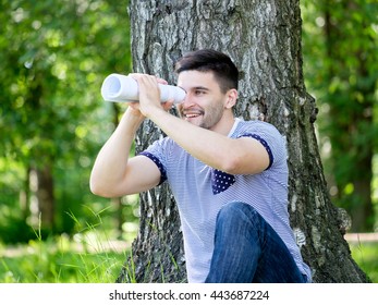 Young Man Looking Through The Book Like Spyglass In City Park