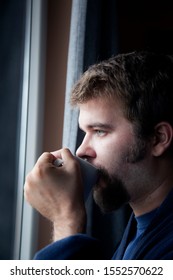 Young Man Looking Through a Window in a Rainy Day, drinking coffee at home
