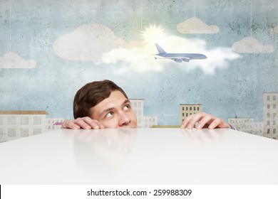 Young Man Looking From Under Table At Flying Airplane