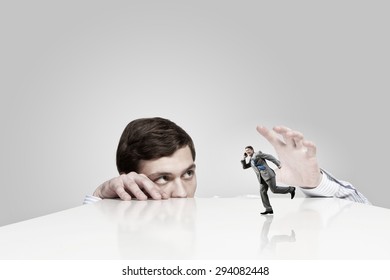 Young Man Looking From Under Table And Catching Running Businessman 