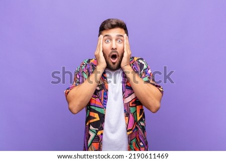 young man looking unpleasantly shocked, scared or worried, mouth wide open and covering both ears with hands