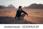 Young man looking upon the vast desert of Wadi Rum in Jordan, after sunset. 