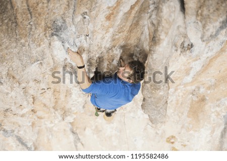 Young man looking up while climbing challenging route on cliff.