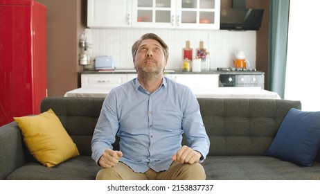 Young man looking up while sitting on a comfortable sofa in his apartment. Creative people can put whatever they want where the man points. 
